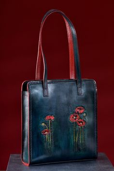 "Hand tooled leather bag with red poppies. The bag has very interested peacock blue color wtih dark and light tints. When dyeing  the leather, we set the shades of several colors. Combining this background with hand tooled  red poppies produces an interesting and beautiful texture. The bag closes with a zipper.  Whole bag is hand stitched (including shuolder straps). Shoulder straps made from two layers leather which are connected with hand stitching. Upper layer made from thick and qualitative leather and backside from goatskin. The liner of the bag is from red \"Greta\" lining fabric.  The product is coated with finish wax, which prolongs moisture protection and contamination. Тhis is a very comfortable and spacious bag for any occasion. It looks elegant and casual at same time. 5 leathe Red Hand Painted Bags, Hand-painted Leather Tote Shoulder Bag, Hand Painted Leather Tote Shoulder Bag, Rectangular Hand Painted Bag, Elegant Hand Painted Rectangular Bag, Luxury Handmade Blue Bags, Elegant Hand Painted Rectangular Bags, Luxury Hand-painted Leather Bags, Luxury Hand Painted Leather Bags