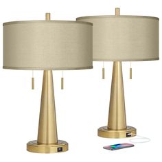 two gold table lamps next to each other with a cell phone plugged into it