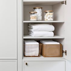 an organized closet with white linens, baskets and other items in gold lids on the shelves