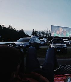 two people sitting in the back of a car watching a movie on a large screen