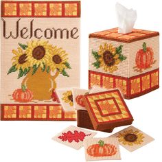 a cross stitch kit with sunflowers and pumpkins on it, next to a tissue box