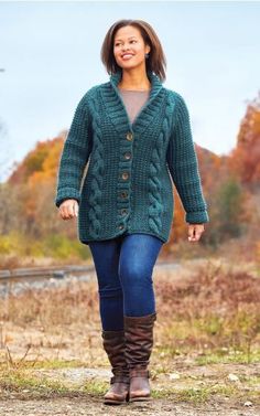 a woman walking down a dirt road wearing boots and a green cardigan sweater with buttons