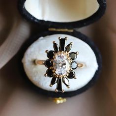 an engagement ring with black and white stones sits in a box on top of a table