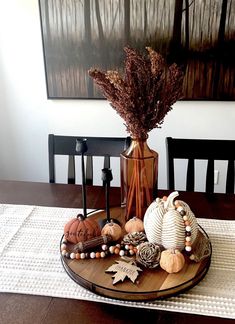 a wooden tray with pumpkins and other decorations on it sitting on a dining room table