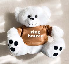 a white teddy bear wearing a brown ring bearer t - shirt with black paws on it