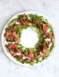 a white plate topped with a salad covered in greens and meats on top of it