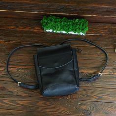 a black leather purse sitting on top of a wooden floor next to a green plant