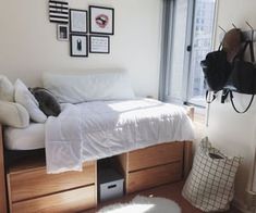 a bedroom with white bedding and wooden drawers in front of a window overlooking the city