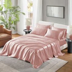 a bed with pink sheets and pillows in a living room next to a couch, chair and window