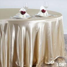 two wine glasses sitting on top of a table covered in a gold cloth with red rose centerpieces