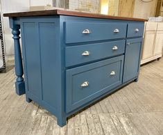 a blue kitchen island with wooden top in a room filled with cabinets and other furniture