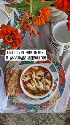 a bowl of soup is sitting on a plate with bread and flowers in the background