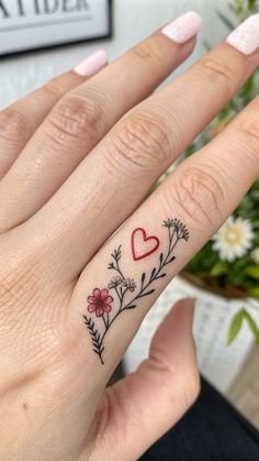 a woman's hand with a heart and flowers tattoo on the middle ring finger