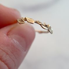 a person holding a tiny gold ring with leaves on it's side, in front of a white background