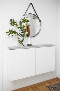 a vase with flowers on top of a white cabinet next to a mirror and rug