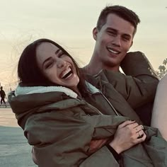 a man holding a woman in his arms and smiling at the camera while she holds her