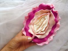 a hand holding a pink and white flower on top of a white cloth covered bed