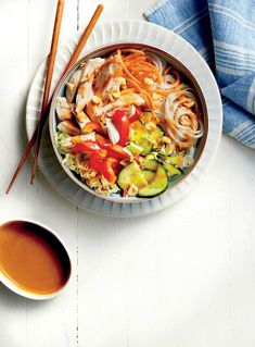 a white plate topped with noodles and veggies next to chopsticks on a table