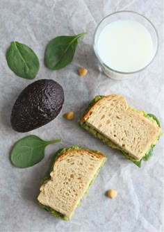 an avocado and two sandwiches are next to a glass of milk