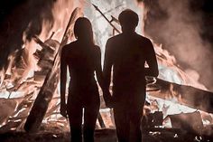 two people standing next to each other in front of a fire