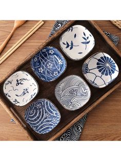 six blue and white plates in a tray with chopsticks next to them on a wooden surface