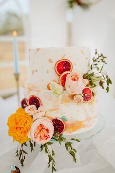 a wedding cake decorated with fresh flowers and oranges sits on a white tablecloth