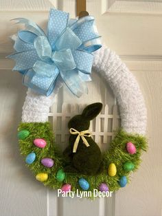 a green bunny wreath with blue bow and eggs in front of a white door decorated for easter