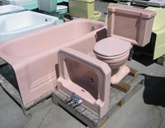 two pink toilets sitting next to each other on pallets in front of tubs and sinks