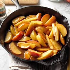 a frying pan filled with sliced apples on top of a table next to utensils