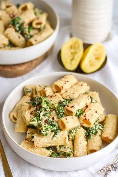 two bowls filled with pasta and spinach on top of a white table cloth next to sliced bananas