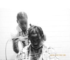 two young children blow drying their hair in front of a white brick wall, one boy with dreadlocks on his head