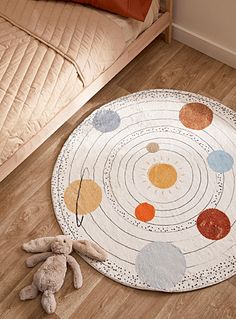 a teddy bear sitting on the floor in front of a round rug with colorful circles