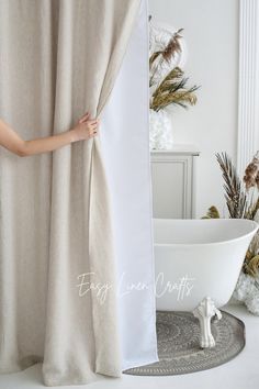 a white bath tub sitting next to a window covered in beige linens and curtains