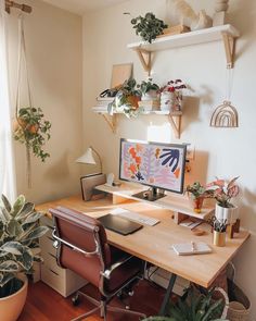 a desk with a computer on top of it next to a potted plant in front of a window