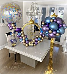 a table with balloons and decorations on it in a room that has white walls, wooden floors and a chandelier