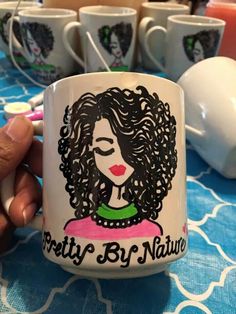 a person holding a coffee mug with the words pretty by nature on it in front of some cups