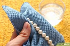 a hand holding a blue cloth with pearls on it and a glass in the background