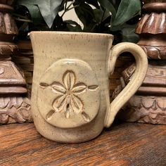 a coffee cup with a flower on it sitting on a wooden table next to a potted plant