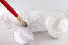 a red and white paintbrush sitting on top of a piece of paper next to a cup