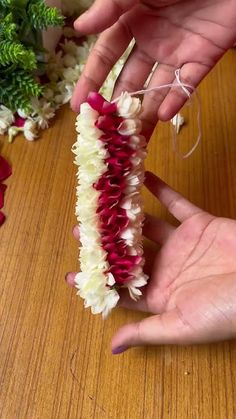 two hands are holding some flowers on a wooden table and another hand is reaching for the flower