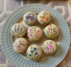 six painted eggs on a plate with flowers and leaves in the middle, sitting on a tablecloth