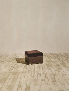 a square foot stool sitting on top of a hard wood floor next to a wall