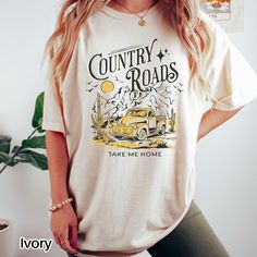 Check out our cute retro country shirt with the graphic and words Country Roads Take Me Home! Size up one size for an oversized look, and size up two sizes for the t-shirt dress look.  Refer to the sizing picture for more details on measurements. Comfort Colors introduces its garment-dyed t-shirt; a fully customizable tee made 100% with ring-spun cotton. The soft-washed, garment-dyed fabric brings extra coziness to your wardrobe while the relaxed fit makes it an excellent daily choice. The doubl Country Style Graphic Print T-shirt For Spring, Spring Country Style T-shirt With Graphic Print, Country Style White Top With Graphic Print, Vintage Slogan Shirt For Summer, Relaxed Fit Country Style Crew Neck T-shirt, Country Style Crew Neck Top With Graphic Print, Cotton Tops With Letter Print For Country Concerts, Vintage Short Sleeve T-shirt For Country Concerts, Country Style White Graphic T-shirt