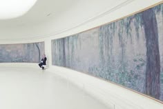 an empty room with paintings on the wall and a person sitting in front of it