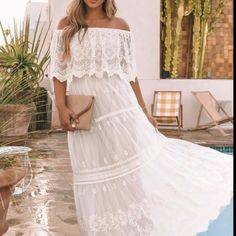 a woman standing in front of a pool wearing a white dress and holding a purse