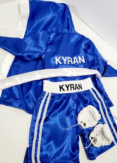 a blue and white boxing outfit with the name kyran on it, next to an open pair of gloves