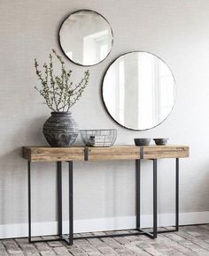 two round mirrors on the wall above a wooden table with vases and plant in it