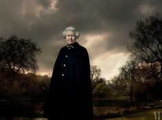 an old woman standing in front of a body of water with trees and clouds behind her