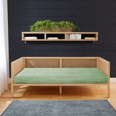 a day bed with a green mattress in front of a black wall and wooden shelves