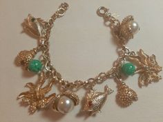 Vintage signed charm bracelet with beach theme charms. This bracelet is designed in gold tone metal and it features sea-side theme charms including fish, seaweed, shells, shell with white faux pearls and green beads. The charms are attached to a cable-link chain that measures 7" long and it fastens with a spring-ring clasp. The clasp has a diamond-shaped hang-tag that is stamped "SARAH COV.".  The gold tone finish is in excellent condition. Sea Charm Bracelet, Ocean Charm Bracelet, Adjustable Gold Charm Bracelet With Starfish Charm, Vintage Charm Bracelet With Lobster Clasp, Ocean-inspired Starfish Charm Bracelet, Gold-tone Metal Charm Bracelet With Vintage Charm, Hang Tags, Green Bead, Gold Tone Metal